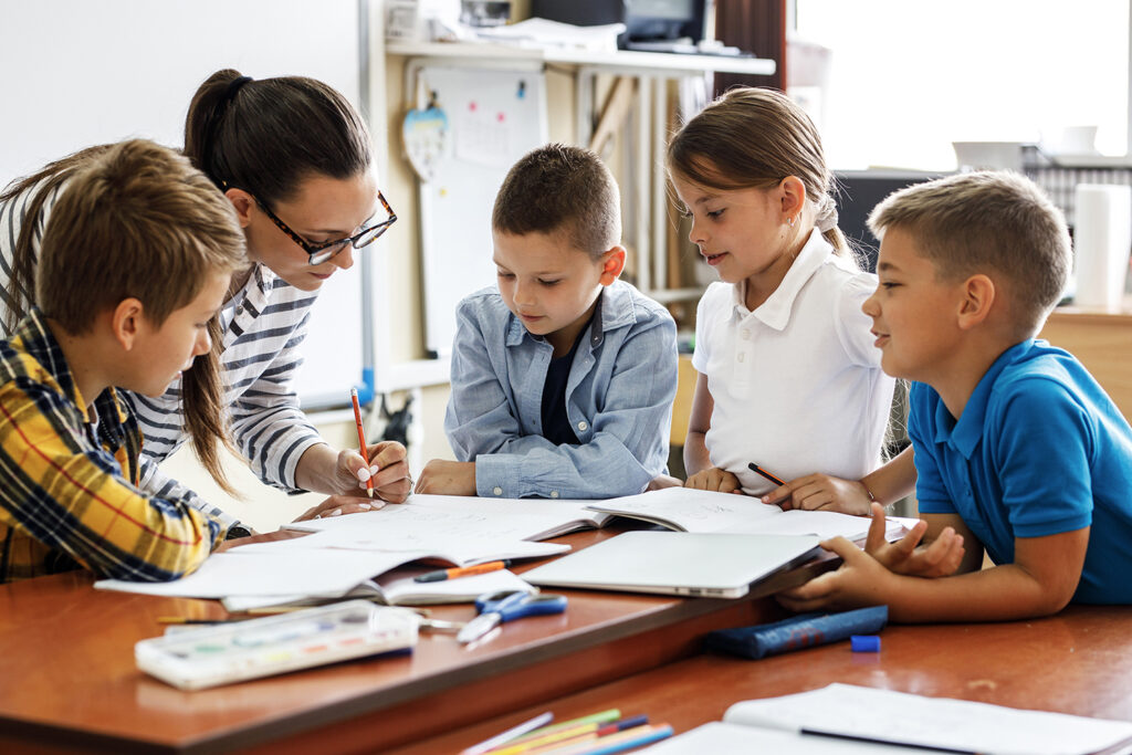 Eine Lehrerin oder Betreuerin gibt Grundschulkindern in Ludwigsburg Hausaufgabenhilfe an einem großen Schreibtisch.