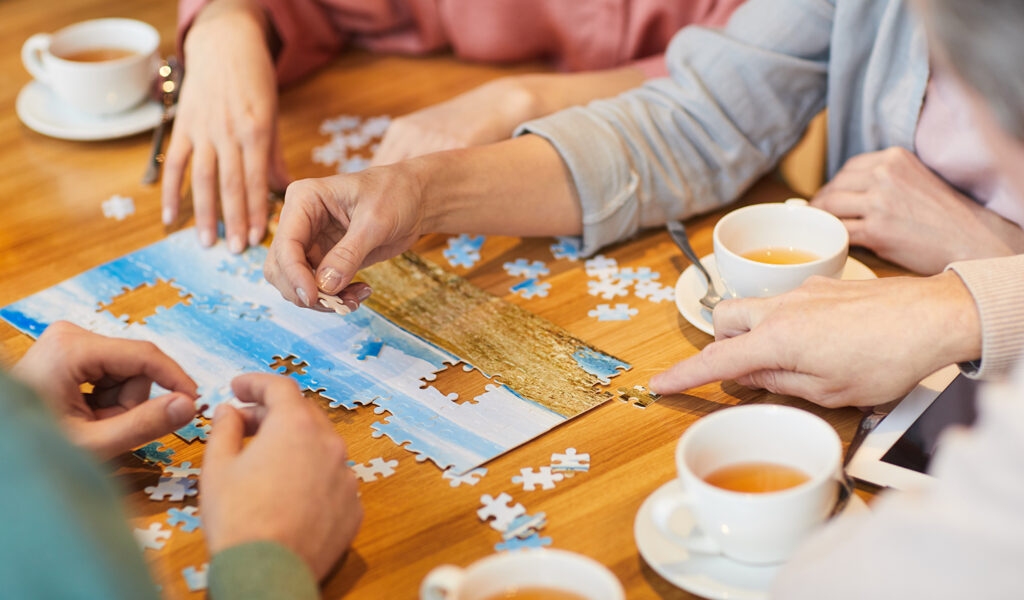 Mehrere Personen puzzeln gemeinsam an einem Holztisch, auf dem Kaffeetassen stehen, beim Spiele- und Kaffeenachmittag in Ludwigsburg.